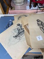 Photo showing multiple charcoal and crayon figure sketches and studies scattered. Visible seated and standing figures, some on beige paper with signs of wear.