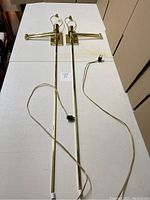 Pair of solid brass wall-mounted swivel arm lamps laid side by side showing full length and attached cords.