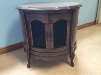 Front view of the wooden cabinet showing double doors with metal mesh panels and decorative handles, curved front and carved legs.