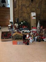Wide view of all Christmas decorations displayed on floor in front of stone wall, including wreaths, nutcrackers, nativity scene, figurines, and bins of ornaments and ribbons.