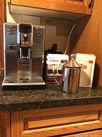 Saeco stainless steel espresso machine front view with maintenance kit box and milk pitcher