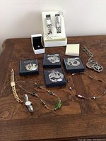 Full view of all jewelry items on wooden surface including watches, ring, bracelets, necklaces, pins, and keychain.