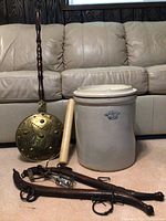 Photo showing the full lot including crock, brass bed warmer, rolling pin, and leather harness straps on carpet in front of a couch.