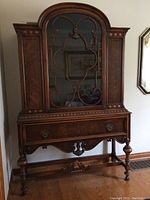 Front view of the wooden display cabinet, showing detailed glass door and drawer below.
