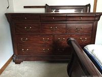 Front view of the wooden dresser showing the multiple drawers, brass handles, and dark wood finish.