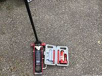 Hydraulic floor jack fully assembled and upright on pavement with long handle.