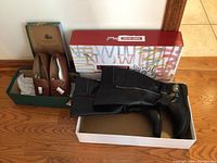 Brown Tender Tootsies loafers and black Dockers knee-high boots in their respective boxes on a wooden floor.