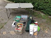 Full view of lot including folding table, tackle box, fishing rods, chair bag, boxed Coleman item, MaxFli glove pack, and ring toss game set.