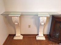 Full view of the glass top table with two white decorative pillars supporting it.