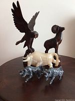 Full view of all five animal figurines on round wooden table including eagle, ram, cream bull, and two small gray bulls.
