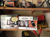 Photo of lower shelf showing two boxed items placed side by side - Black & Decker router box and Connected by TCP LED light bulbs box with a remote control image.