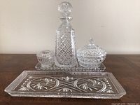Full set of crystal barware on surface showing all items: decanter, lidded jar, small bowl, and rectangular tray.