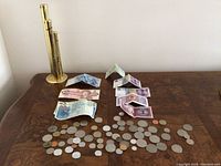 Wide view of used currency notes and coins arranged in two rows on a wooden surface, showing denominations and colors of bills and the condition of coins.