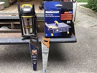 Three items on a metal truck bed: Stanley wet/dry vacuum on left, two hand saws leaning vertically, boxed Mastercraft wet tile saw behind.