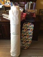 Taller view showing roll of white fabric, small ironing board with patterned cover, and sewing area with containers in background.