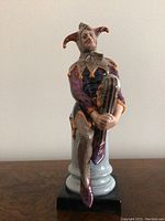 Front view of Royal Doulton The Jester figurine seated on its pedestal showing full figure and facial expression.
