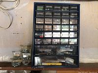 Full view of the blue hardware organizer with many small drawers holding screws and hardware items alongside plastic containers with screws.