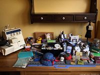 Wide view of sewing machine and assorted sewing supplies on table with wooden background shelf excluded from sale