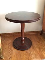 Full view of round pedestal table on wood floor against white wall