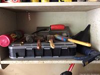 Shelf with assorted masonry and painting tools including trowel, brushes, hammer, putty knife, dustpan with brush, and container of nails.
