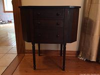 Front angle view of wood cabinet with side compartments closed, showing overall shape and turned legs.