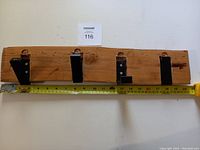 Full frontal view of wooden wall hook with four black metal foldable hooks, measuring tape showing approximately 20 inches length.