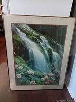 Front view of the large framed waterfall print resting against a wall, showing the entire artwork clearly with visible colors and frame details.
