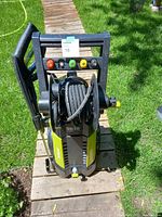 Front view showing unit upright on wooden walkway, four colored nozzles mounted on frame, coiled high-pressure hose on top reel