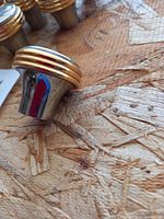 Single metal cabinet knob showing silver tone body with gold ring accent on a textured wood surface.