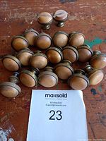 Photo of 20 wooden cabinet knobs with brass rims on a wooden table, showing top and side views.