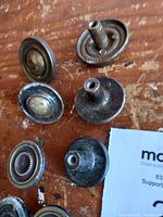 Close-up view of six antique cabinet knobs in various designs and patinas placed on a wooden surface, some inverted to show threaded attachment stems.