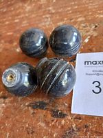 Four black marble cabinet knobs, three smooth and rounded, one with carved groove detail, placed on wooden surface with lot tag.