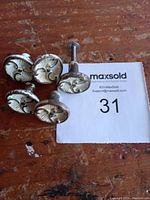 Five antique-style cabinet knobs with raised designs placed on a wooden surface with the MaxSold lot number card