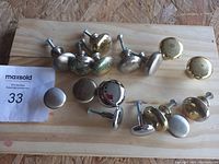 Overview photo showing 16 cabinet knobs in mixed metals including brass and chrome on a wooden board.