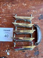 Six cabinet pulls laid on a wooden surface, five brass pulls and one iron pull.