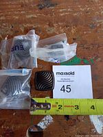 Four vintage brass cabinet pulls in individual plastic bags shown on a wood surface with a measuring tape and MaxSold auction card.
