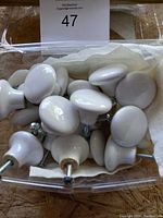 Top view showing 23 white porcelain cabinet knobs in a clear container with some knobs overlapping each other.