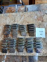 Top-down view showing 45 metal cabinet hinges arranged in rows on a wooden surface with some wear.