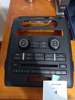 Front view of black plastic dashboard control panel with knobs, buttons, and cutouts for display or media slot.