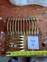 Full lot of 18 brass drawer pulls on wooden surface with measuring tape for scale