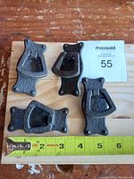 Top view of four antique brass cabinet pulls arranged on a wooden board with a measuring tape showing size approximately 3.5 inches tall each.