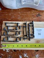 Set of 11 antique brass cabinet pulls laid on wooden board with measuring tape showing length of pulls.