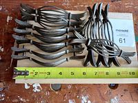 Group photo showing 11 antique brass cabinet pulls laid on a wooden surface with a measuring tape indicating length around 7 inches