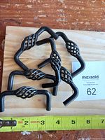 Six black metal antique cabinet pulls arranged on a wooden board with a measuring tape showing about 4 inches wide.