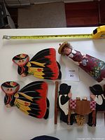 Four Halloween decorations shown, including two large witch cutouts, one small witch figurine, and one wooden carving of figures at a table.