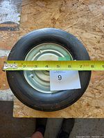 Top view showing one solid rubber wheel with tape measure indicating approximately 8 inches diameter.