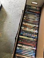 Top-down photo of a large box filled with over 40 DVD cases stacked vertically, showing a variety of movies.