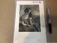 Full view of antique print with woman sitting in dress, mounted in protective sleeve with Sharpie pen for scale.
