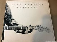 Photo of the front cover of the Eric Clapton Slowhand vinyl album showing the close up image of Eric Clapton's guitar and hand and the text 'Eric Clapton Slowhand'.