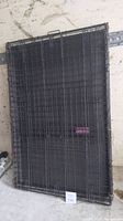 Folded large black metal wire dog crate with plastic tray at base placed against a wall.